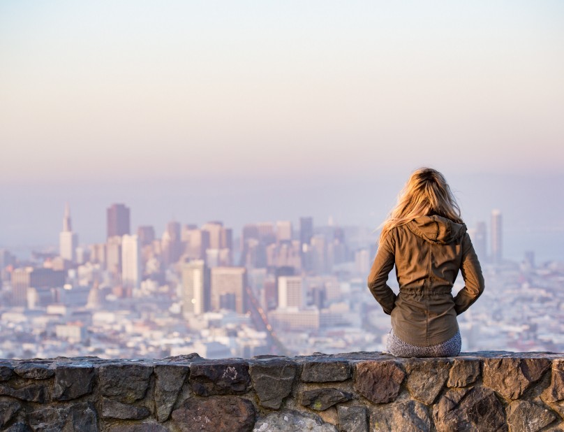 Frau sitzt auf Steinmauer mit Stadt im Hintergrund