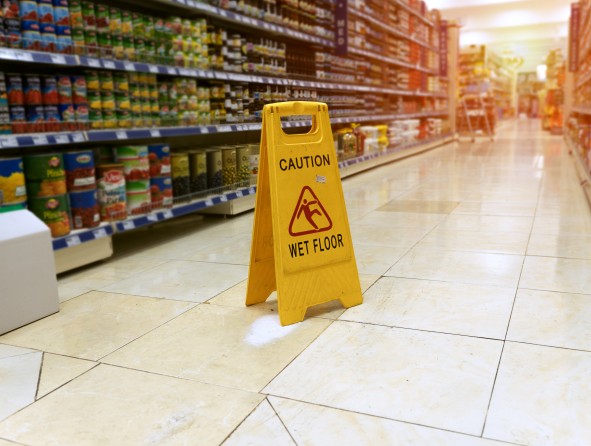 Yellow sign - caution. Wet floor is in the supermarket against the background of blurry products standing on the shelves