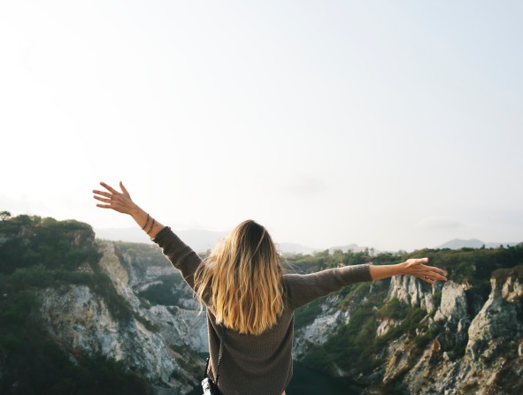 Frau mit geöffneten Armen vor Felsen